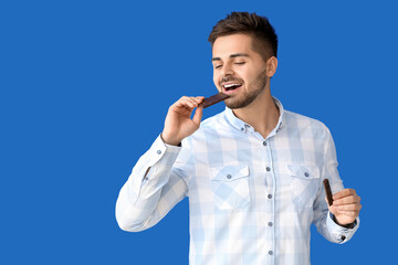 Wall Mural - Handsome young man with tasty chocolate on color background