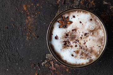 Homemade spicy hot chocolate with anise star, cinnamon sticks and bitter chocolate, dark brown concrete background. Top view. Copy space.