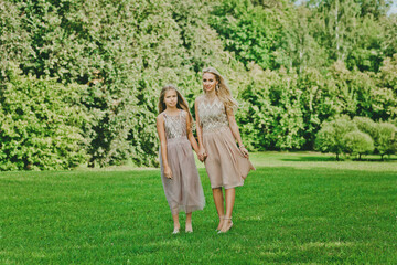 Two adorable blonde girls walking in park on a sunny summer day.  Outdoor photo of happy sisters posing on nature background. 