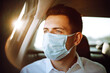 © maxbelchenko - Man passenger in protective sterile medical mask in the taxi car during an epidemic in quarantine city. Health protection, safety and pandemic concept. Covid - 19.