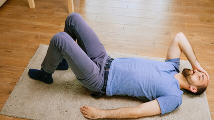 Man with a headache laying on the floor during covid-19 isolation.