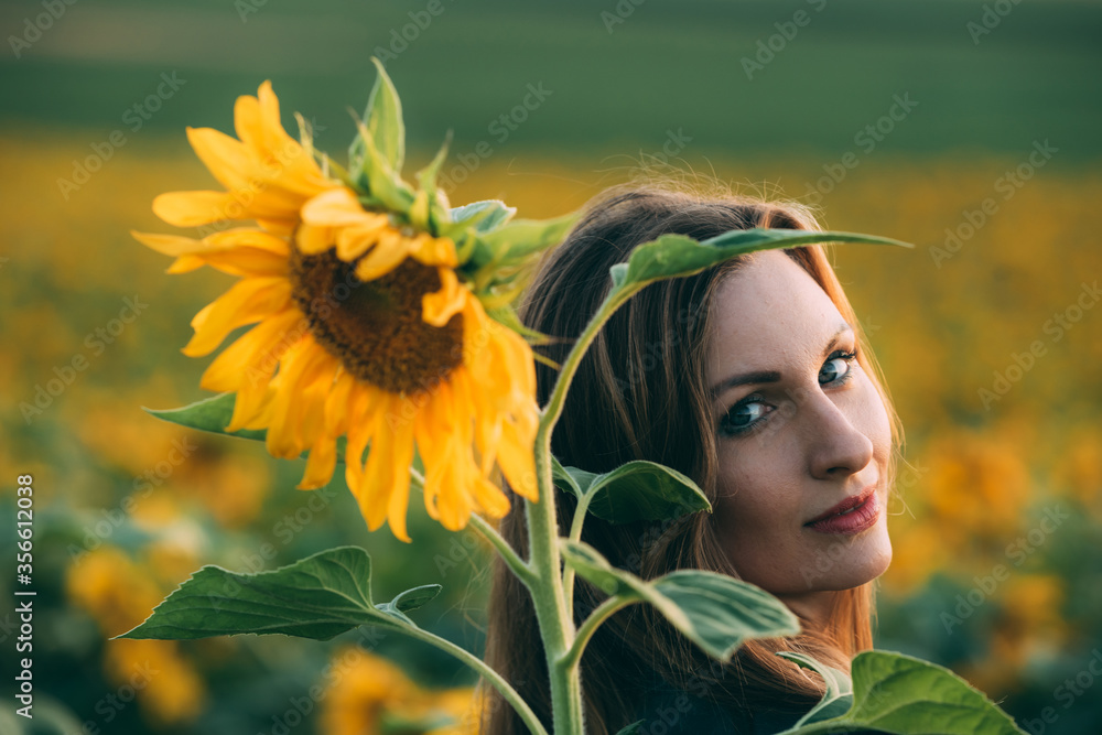 Girl in a green dress and long blond hair in a sunflower field, smiles ...