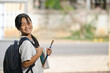 © Prathankarnpap - A schoolgirl is holding painting equipment and carrying a school bag while standing and waiting for a school bus.
