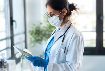beautiful female doctor wearing a hygienic face mask and protective gloves while using her digital t