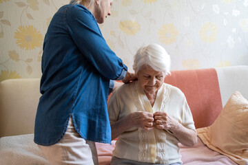 Woman helping senior woman dress in her bedroom
