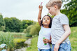 © Iryna - Happy multiethnic different age kids outdoor in summer. Curly cute positive hispanic girl be measured her blond boy friend at lake side in park. Summer, childhood, leisure, lovely people concept