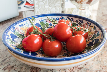 Beautiful organic tomato bunch in a colorful spanish glass salad bowl. Ready to be prepared for a delicious fresh salad or recipe. Marble table.