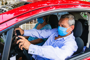 An old man with a medical mask in the driver's seat of the car. Driving to the hospital during the Coronavirus pandemic concept