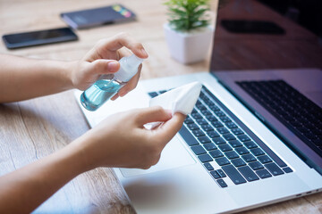 Woman cleaning laptop and smartphone by wet wipes tissue and alcohol disinfectant on workplace during work at home, protection coronavirus (Covid-19) infection. New Normal and Clean surface concept