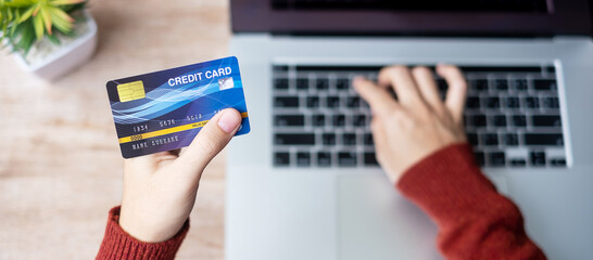 woman wearing sweater holding credit card and using laptop for online shopping while making order at home office. business, lifestyle, technology, ecommerce, digital banking and online payment concept