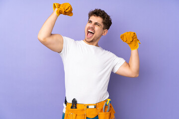 Wall Mural - Young electrician man over isolated on purple background celebrating a victory