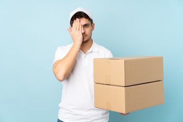 Wall Mural - Delivery caucasian man isolated on blue background covering a eye by hand