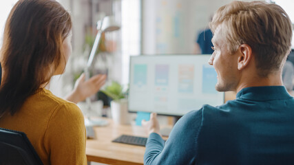 Two Mobile Software Developers Work on Desktop Computer, They Discuss Smartphone Application Design. In the Background Modern Stylish Office with Diverse Team of Professionals.