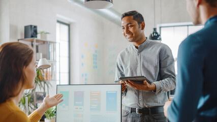 Three Mobile Software Developers Work on Desktop Computer, They Discuss Smartphone Application Design Use Touch Screen Digital Tablet. Modern Stylish Office with Diverse Team of Professionals Working.