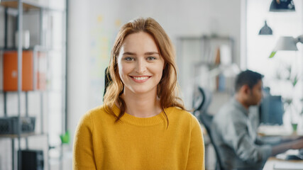 Wall Mural - Portrait of Beautiful Young Woman with Red Hair Wearing Yellow Sweater Smiling at Camera Charmingly. Successful Woman Working in Bright Diverse Office.
