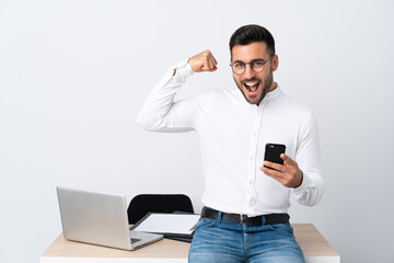 Wall Mural - Young businessman holding a mobile phone making strong gesture