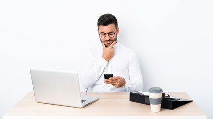 Wall Mural - Young businessman in a workplace thinking and sending a message