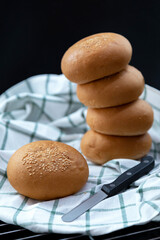 homemade sesame hamburger or burger buns with a butter knife on a striped white kitchen cloth on black background.