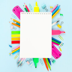 White notebook surrounded by various school office and painting supplies on blue background. Back to school concept. Top view. Copy space