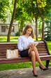 © Andrey_Arkusha - Young business woman in white shirt to go and touch pad during a break sitting outdoors in summer park on the background