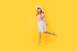 happy girl in a summer hat and sunglasses in summer, jumping high on an yellow background