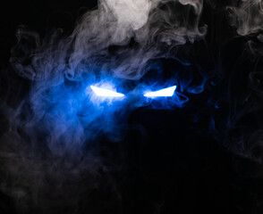 Ominous luminous eyes staring out of the darkness illuminate with rays of blue light swirling white smoke