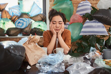 Young Female Thoughtfully Sitting At Table In Her Messy Room