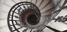 A Spiral Staircase Spiraling Down About Five Floors. The Winding Concrete Stairs Are Empty. The Metal Hand Rail Is Nicely Decorated. The Image Approaches The Golden Ratio And Fibonacci Spiral.