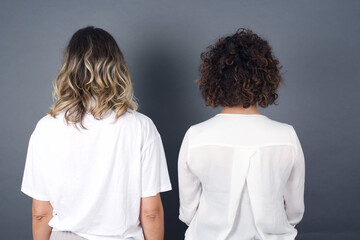 Wall Mural - The back view of a girl with long straight wavy and shiny hair standing against gray wall. Studio Shoot.