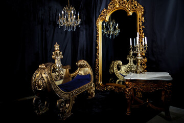 Vintage interior with antique furniture on black background. Old gondola sofa, chandelier and candelabra on table by huge mirror. Gold in black. Copyright space. Large space for inscription or logo