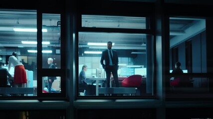 Wall Mural - Footage from Outside the Window: Serious Businessman Walking to an Office Window. Business Managers and Financial Specialists Work in the Background. Employee Answers a Call on Mobile.