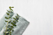 Rolled fluffy towel and green eucalyptus branch on white background. Minimalist scandinavian style. Hygiene, wellness well-being, body care concept. Copy space, top view