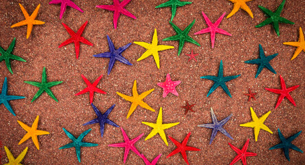 Many multi-colored starfish on red coral sand, top view