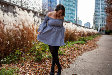 young beautiful fashion Latina woman wearing a trendy blue skirt is enjoying the outdoor park in the Chicago downtown metropolitan area. autumn is here as the color of the trees have change red 