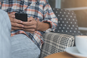 Wall Mural - Man sitting on sofa using mobile smart phone at home