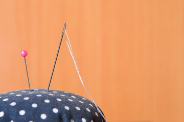 Wall Mural - Needle with white thread and pink pins on pincushion for handmade sewing cloth with brown wood background close-up.