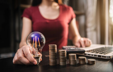 businessman hand holding lightbulb with using laptop computer and money stack in office. idea saving energy and accounting finance concept in office.