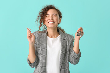 Canvas Print - Happy young woman with key and crossed fingers on color background