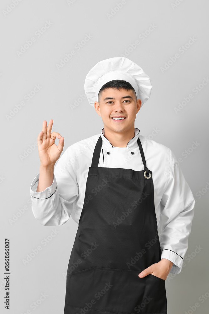 Handsome Asian chef showing OK gesture on grey background