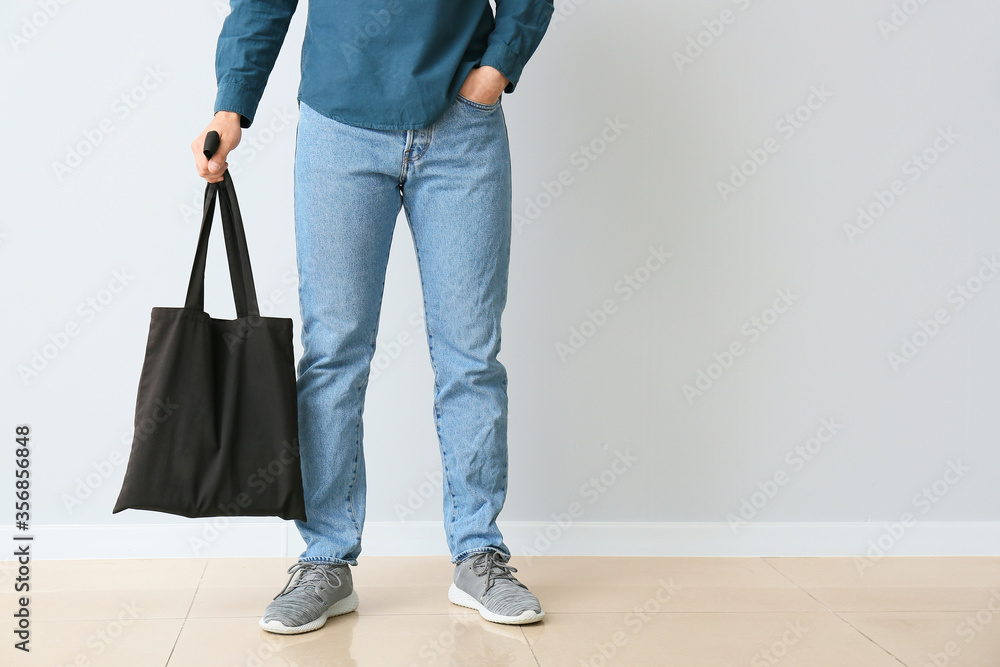 Young man with eco bag against light wall