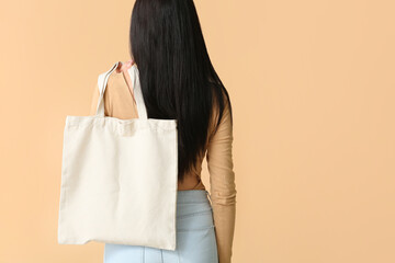 Young woman with eco bag on color background, back view