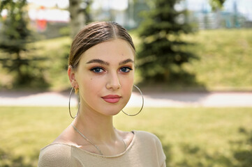 Close-up portrait of a cute caucasian young woman with excellent make-up posing in a city park in sunny summer weather