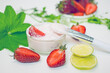 DIY homemade strawberry facial mask. A glass bowl with a pink mass of cream and strawberries next to a sprig of green plants, halves of fresh berries, lime, a brush for applying masks 