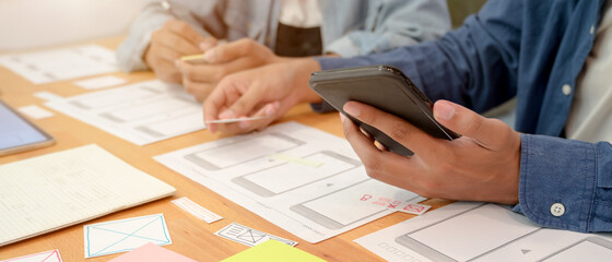 Wall Mural - ui developer team consulting on their project with smartphone and paperwork on wooden table