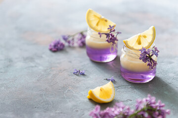 Lilac Vodka Shots drinks with vanilla liqour. Cocktail with Fresh lemon on gray concrete background with lilac flowers. Bar, restaurant menu, recipe. Side view, copy space