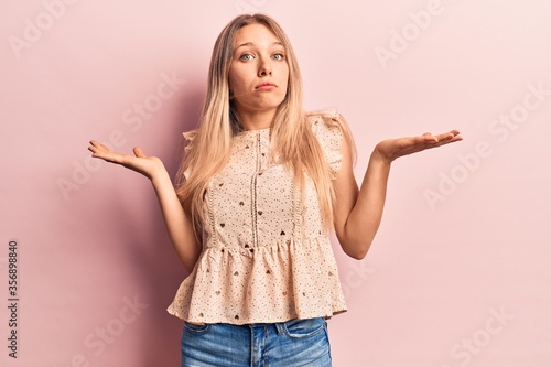 Young blonde woman wearing casual clothes clueless and confused with open arms, no idea and doubtful face Tableau sur Toile