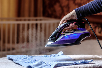 Closeup female hand ironing clothes on the table. Puffs of hot steam break out of the iron. Dark blurred background.