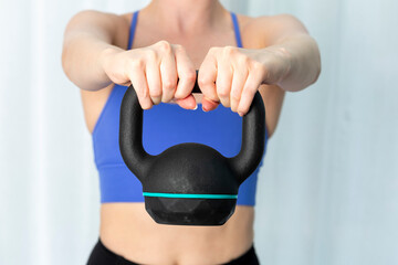 Young woman exercising at home in blue sports top using a kettlebell