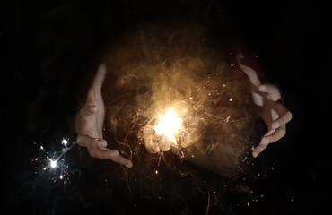 sparkles between female hands trying to capture the light as if a magician in a dark black backgroun