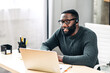 © Vadim Pastuh - Young African-American guy is call center worker or support. Smart black man in eyeglasses uses a handsfree headset and laptop to talk online at his workplace